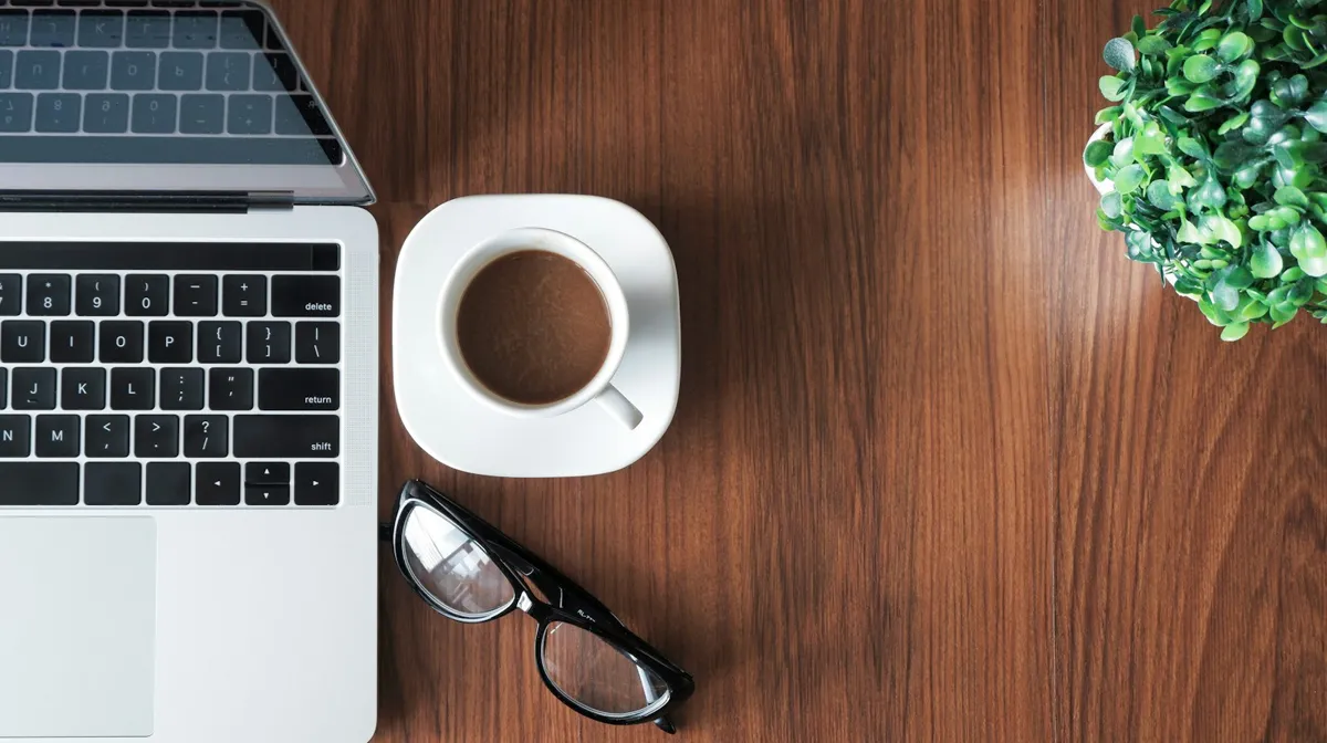 Laptop, coffee cup and glasses on a wooden desk